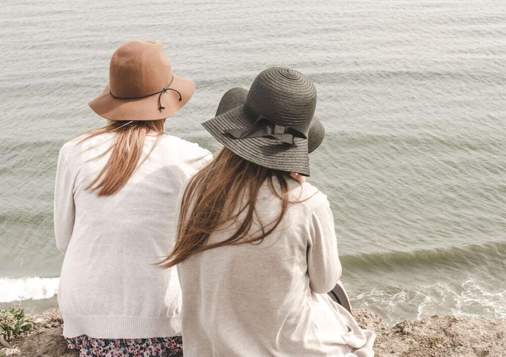 2 individuals with hats on gazing out at the sea