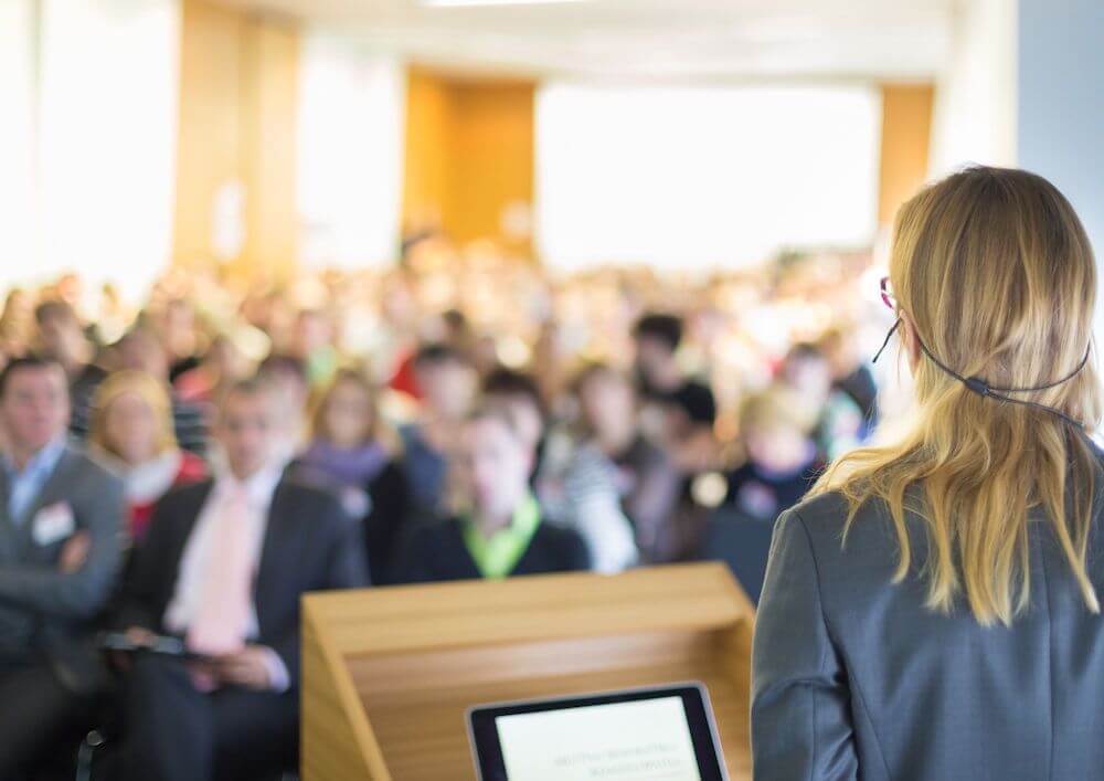 person-standing-at-a-podium-addressing-an-audience