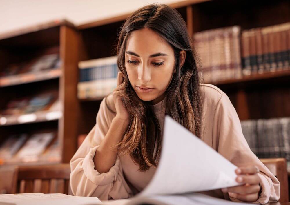 long-haired-individual-browsing-papers-with-bookshelves-behind