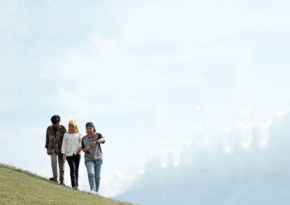 three-individuals-walking-on-a-grassy-slope